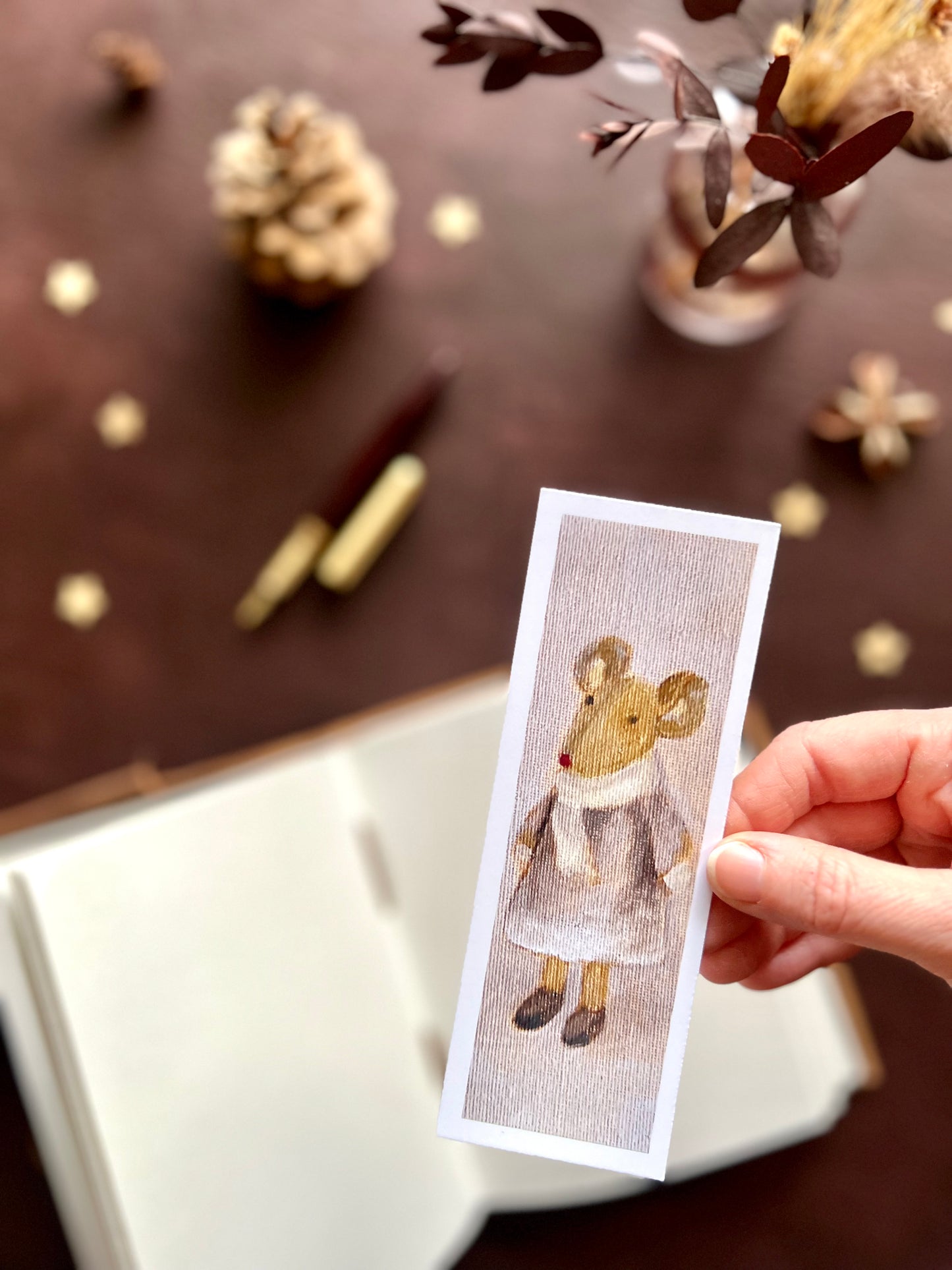 Close-up of a handcrafted bookmark featuring a mouse in a lilac dress, printed oil painting with soft pink background and subtle artistic canvas texture.
