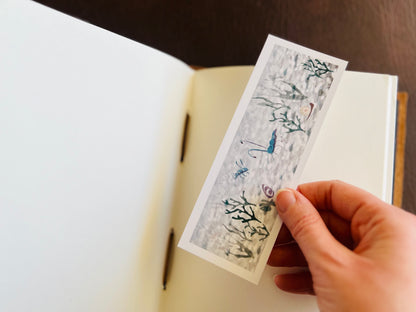 Hand placing the sea-themed ocean bookmark into an open sketchbook.