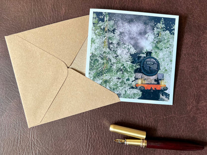 Artisan illustrated Christmas greeting card featuring steam engine 80136 travelling through a snow-covered forest at night with frosted trees and steam rising into the night sky, laid flat on a tabletop. Festive railway-themed winter scene card for train enthusiasts.
