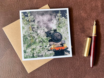 Artisan illustrated Christmas greeting card featuring steam engine 80136 travelling through a snow-covered forest at night with frosted trees and steam rising into the night sky, laid flat on a leatherette tabletop with a fountain pen. Festive railway-themed winter scene card for train enthusiasts.