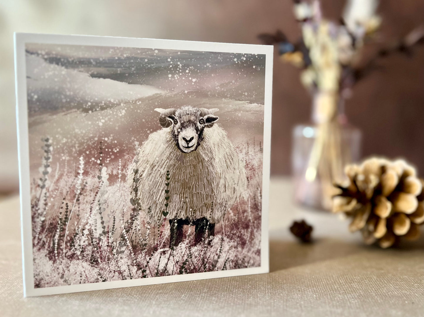 Artisan illustrated Christmas greeting card featuring a Swaledale sheep standing in a snowy Yorkshire Dales countryside landscape, displayed standing upright on a tabletop. Festive winter countryside wildlife design inspired by rural British scenery.
