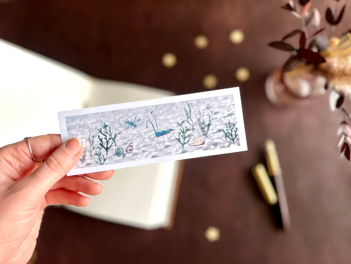 Ocean life bookmark shown with a fountain pen and open sketchbook on a warm cosy writing desk with a creative illustrated stationery aesthetic.