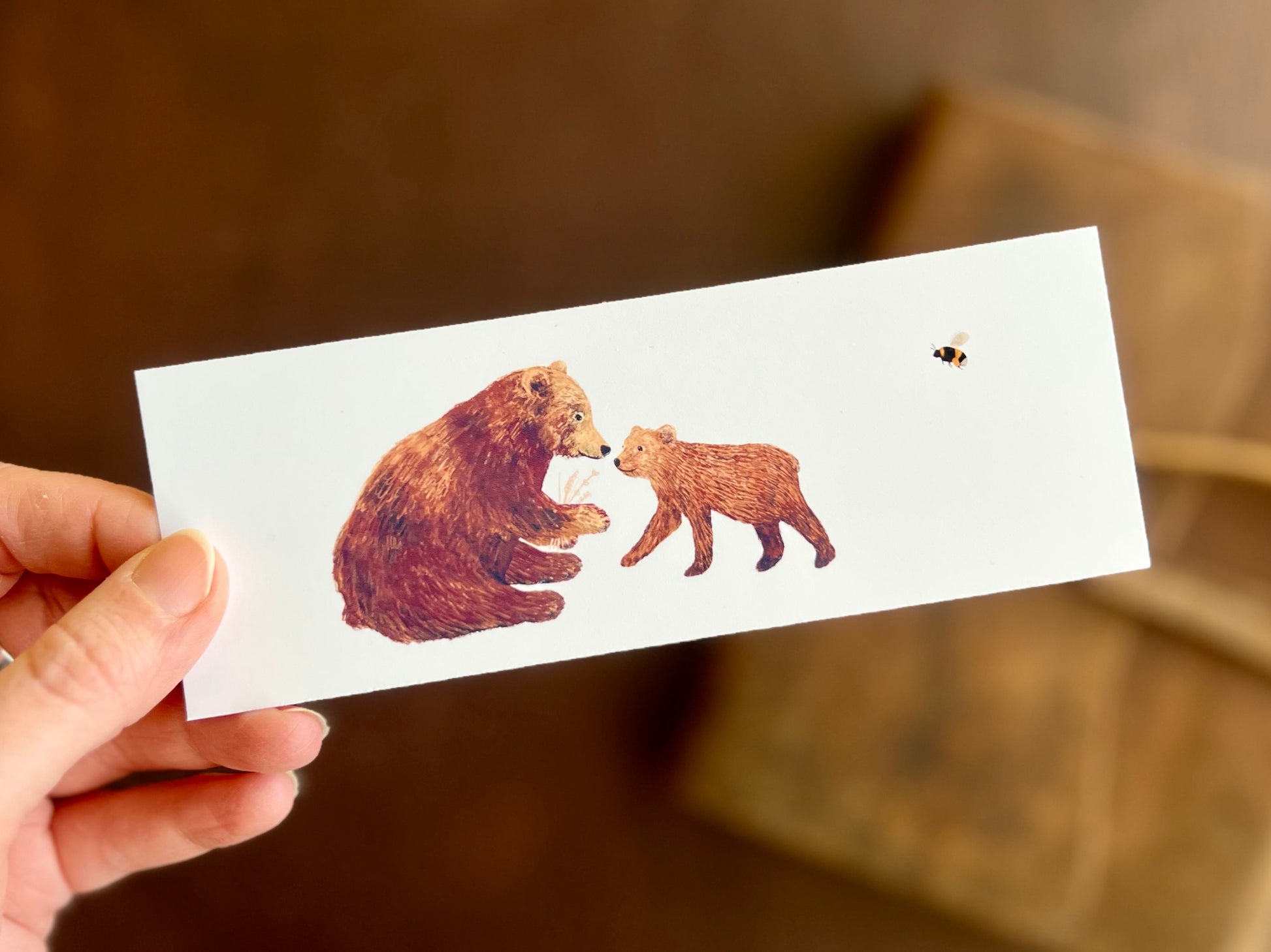 Illustrated bookmark featuring two brown bears and a bee. 