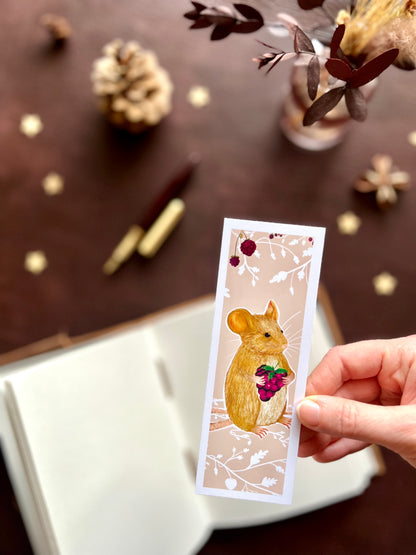 Close-up of a handcrafted countryside mouse bookmark featuring a mouse holding a blackberry on a pinky peach floral background, photographed in a soft nature inspired setting.