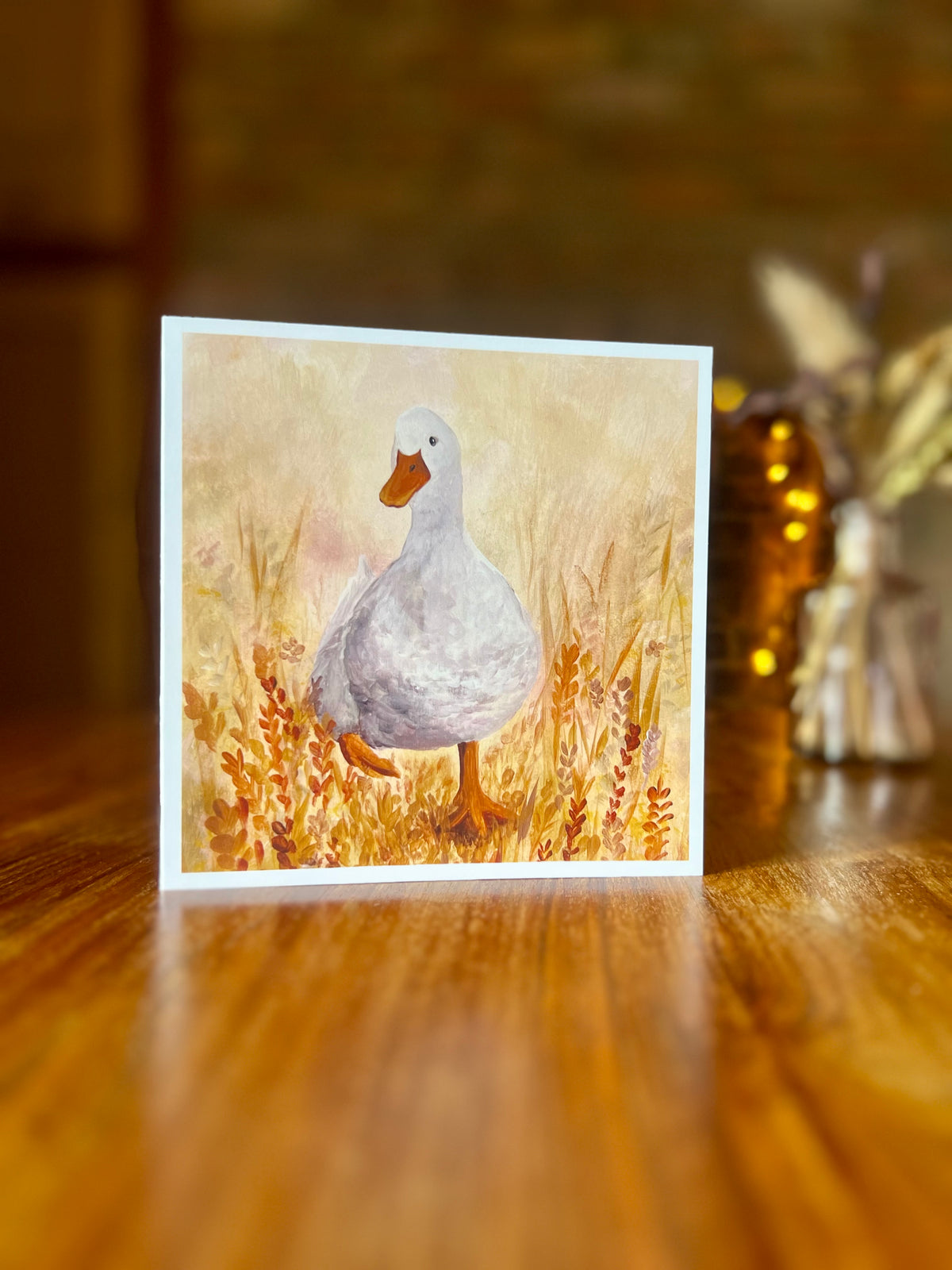 Artist-designed greeting card featuring a print of the original oil painting Duck in the Meadow, showing a characterful white duck waddling through a colourful meadow of yellow and orange flowers in a painterly style with a white border.