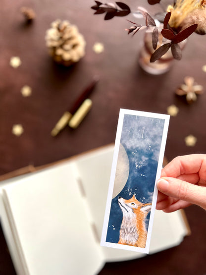 Hand holding a card with a fox design against a blurred decorative background. Dark academia and nature theme.