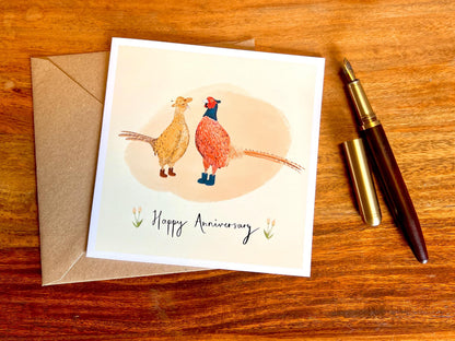 Handcrafted illustrated greeting card laid flat on top of a recycled fleck kraft envelope, positioned next to a fountain pen in a styled flat lay composition. Premium greeting card design highlighting quality materials and presentation.