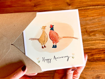 Handcrafted anniversary greeting card with a lemon yellow background featuring an illustrated male and female pheasant in a countryside wildlife theme. Premium illustrated card design supplied with a recycled 110gsm kraft envelope.