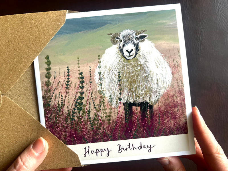 Greeting card with a sheep illustration and 'Happy Birthday' text, held by a person.