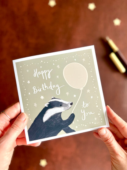 Artisan woodland birthday card with balloon illustration and handwritten typography, photographed with fountain pen in rustic artist studio setting
