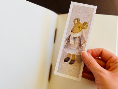 Mouse bookmark being placed into an open sketchbook.