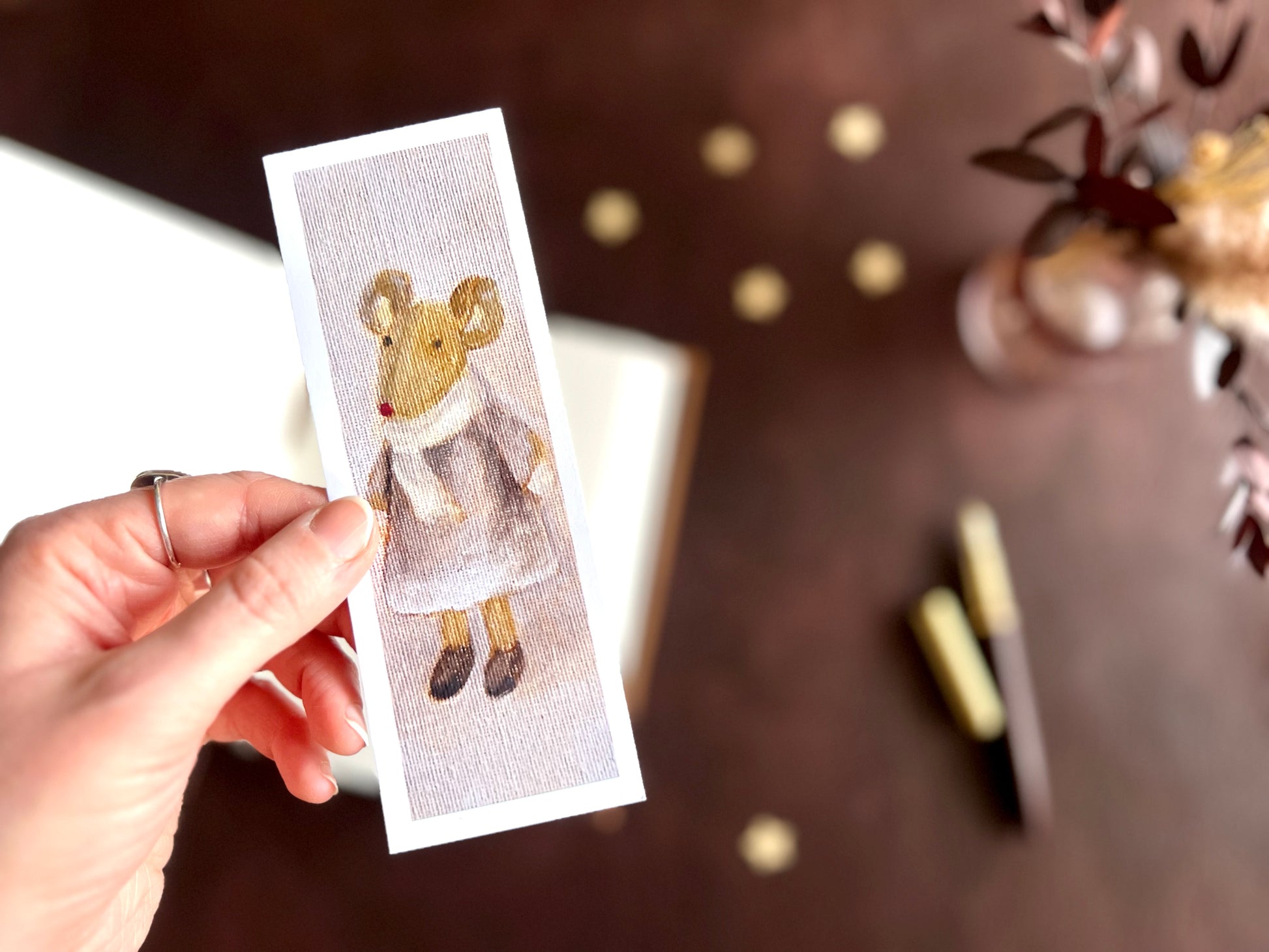 Mouse in a lilac dress bookmark shown with a fountain pen and open sketchbook on a cosy creative desk, highlighting its painterly oil painting style.
