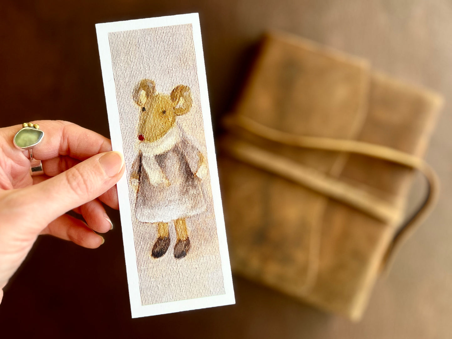 Close-up of a handcrafted bookmark featuring a mouse in a lilac dress on a light pink background, printed from an original oil painting with visible canvas texture.
