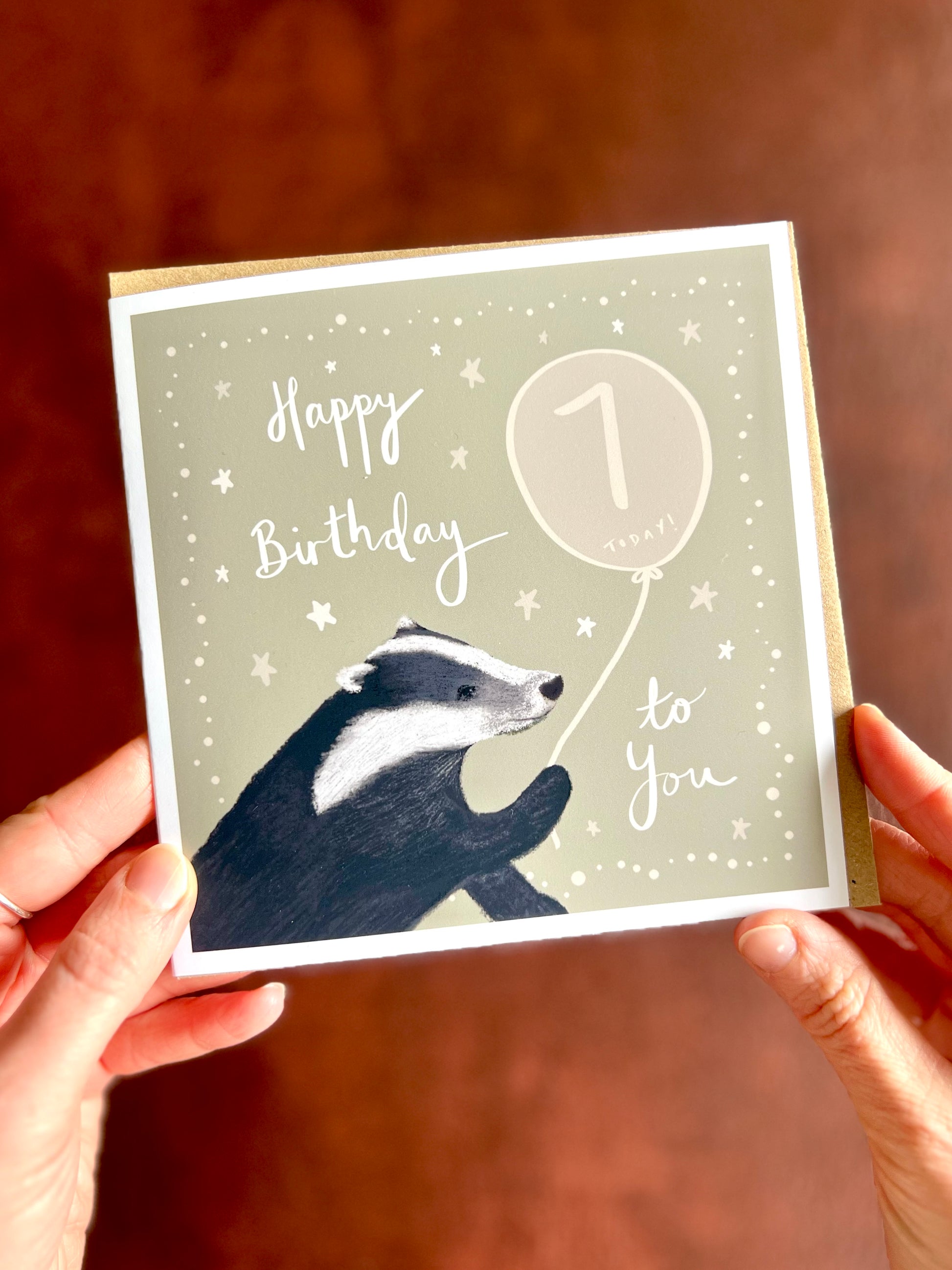 Personalised badger birthday card with green background and illustrated woodland badger holding balloon with custom age 7 today