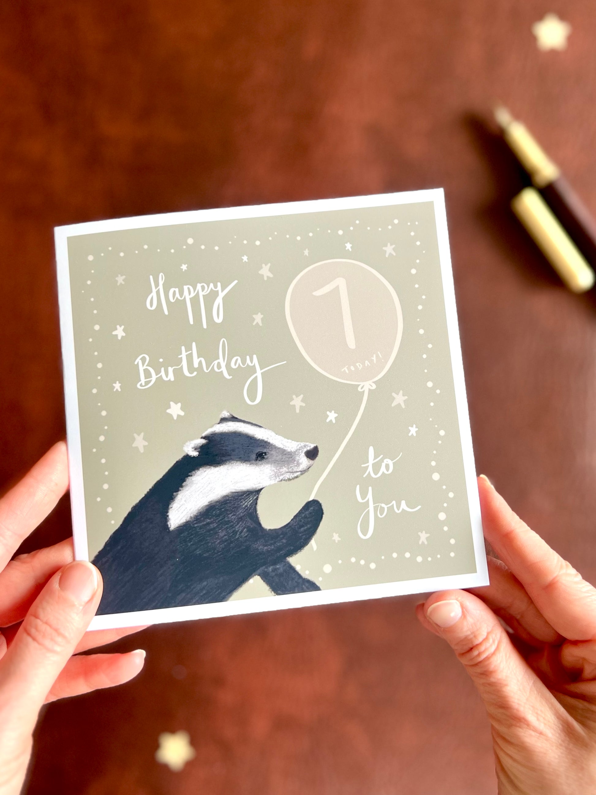 Hands holding personalised woodland birthday card with custom age balloon and illustrated badger design, handmade greeting card with rustic aesthetic, ideal for milestone celebrations and unique birthday gifts