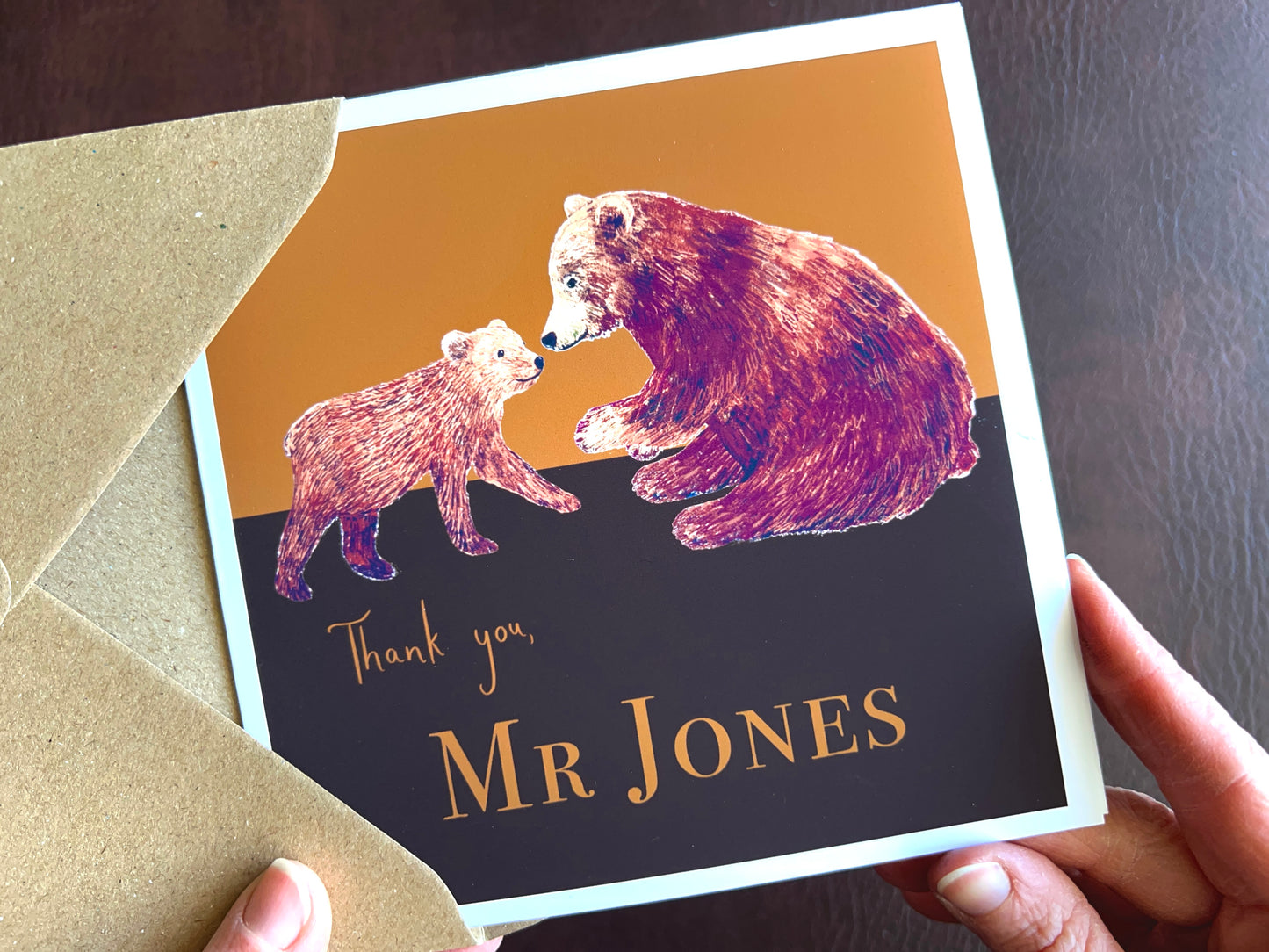 Premium personalised thank you teacher card featuring an illustrated adult brown bear and bear cub against a dark brown and burnt orange background. Example design shown with the text ‘Thank you, Mr Jones’, demonstrating custom teacher name personalisation. Ideal end of term or end of school year thank you card for male or female teachers. Printed on thick 312gsm fine art card by a UK independent artist and supplied with a recycled kraft envelope.