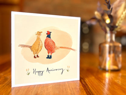 Premium illustrated greeting card displayed standing upright on a rustic wooden tabletop in a lifestyle setting. The image showcases the handcrafted design and quality finish of the card with natural lighting and a simple background.