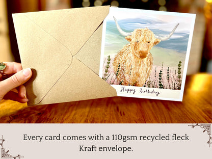 Premium illustrated birthday greeting card featuring a highland cow standing amongst heather in a tranquil countryside landscape, being removed from a recycled fleck kraft envelope. The image highlights that a 110gsm recycled fleck kraft envelope is included with each card, with “Happy Birthday” text beneath the illustration.