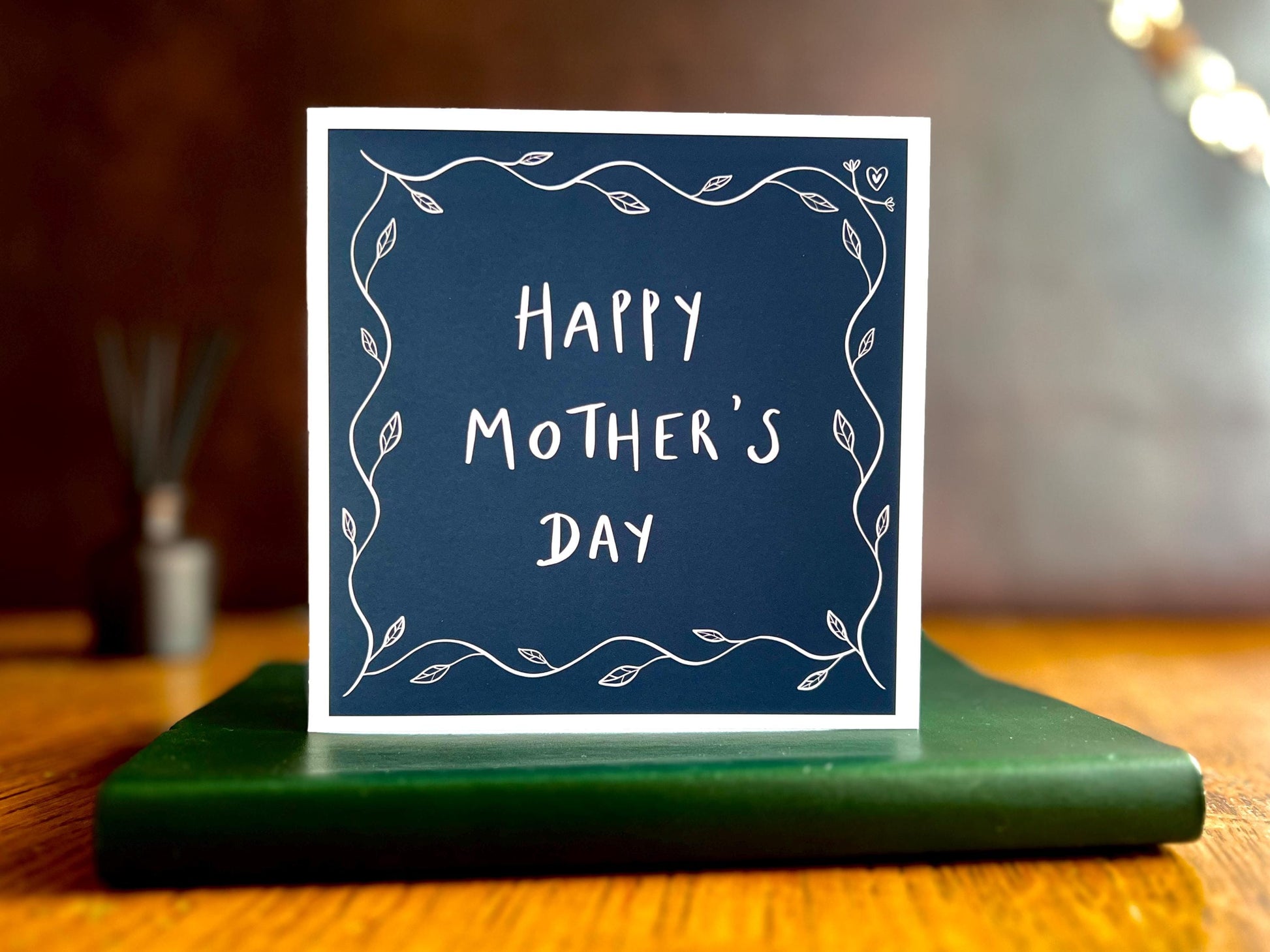 Premium Mother’s Day greeting card with a dark navy blue background and simple leaf border, displayed standing upright on a tabletop. The non-personalised version shows “Happy Mother’s Day” in the centre with optional space for a name underneath.