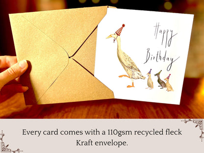 Premium illustrated birthday greeting card featuring a mother runner duck with three ducklings wearing party hats, being removed from a recycled fleck kraft envelope. Text on the image states that every card comes with a 110gsm recycled fleck kraft envelope, highlighting premium packaging and presentation.