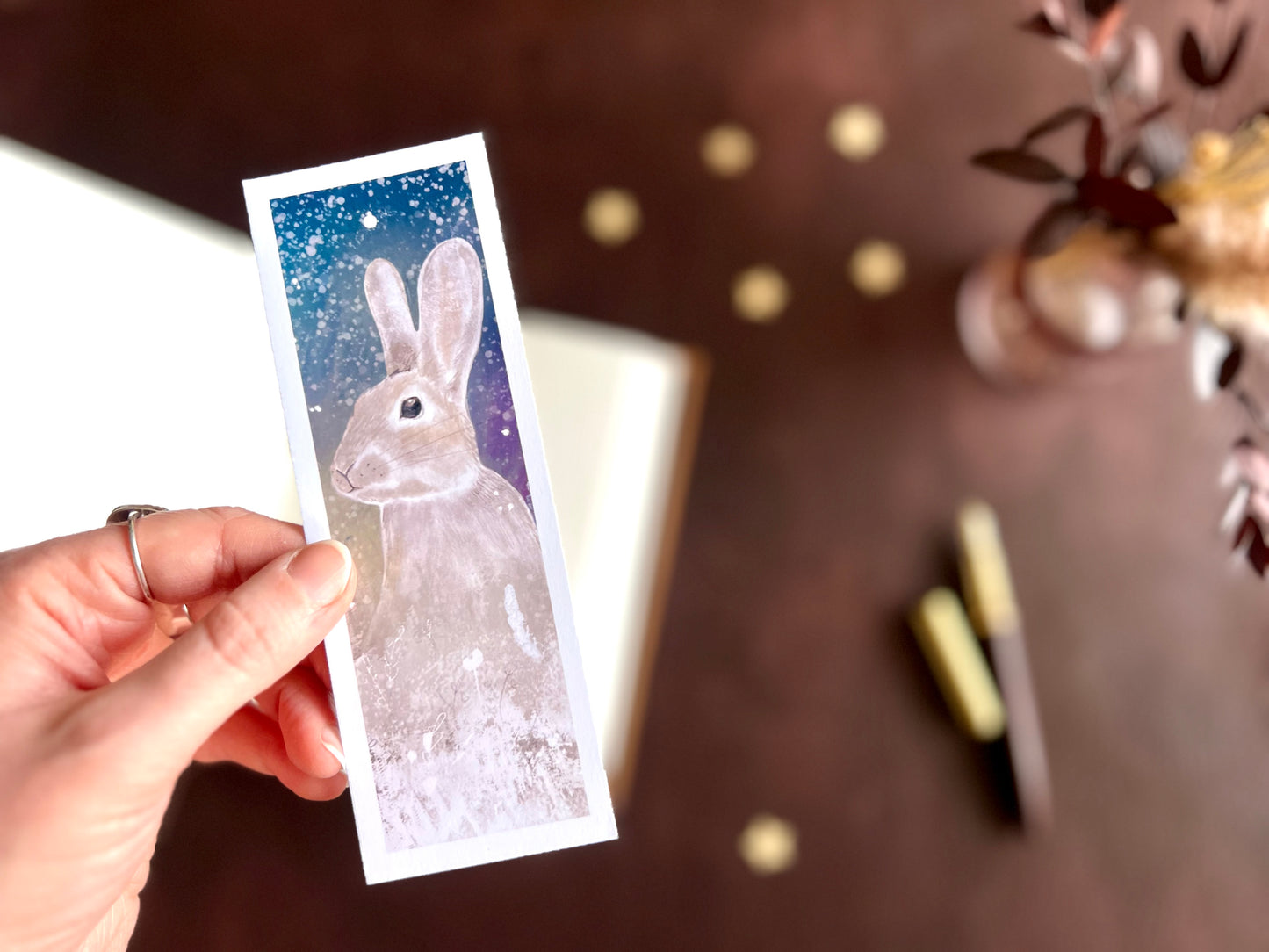 Rabbit celestial bookmark shown with a fountain pen and open sketchbook on a warm cosy writing desk with a magical winter night aesthetic.