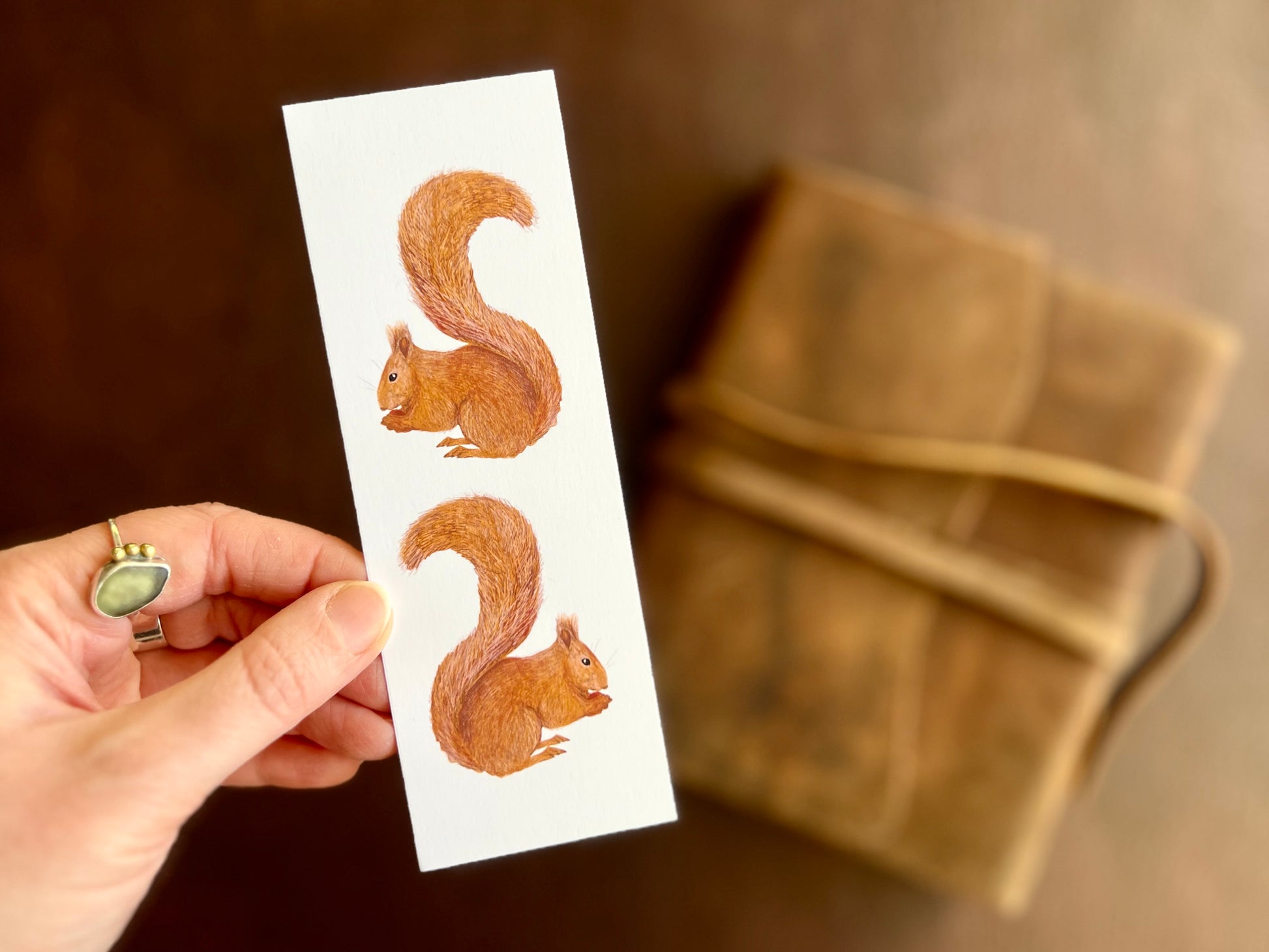 Hand holding a handcrafted red squirrel bookmark featuring two illustrated squirrels on a clean white background.