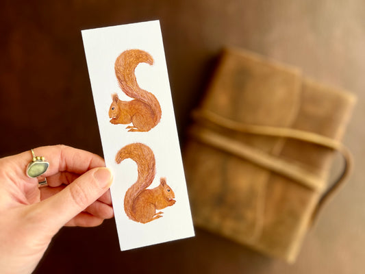 Hand holding a handcrafted red squirrel bookmark featuring two illustrated squirrels on a clean white background.