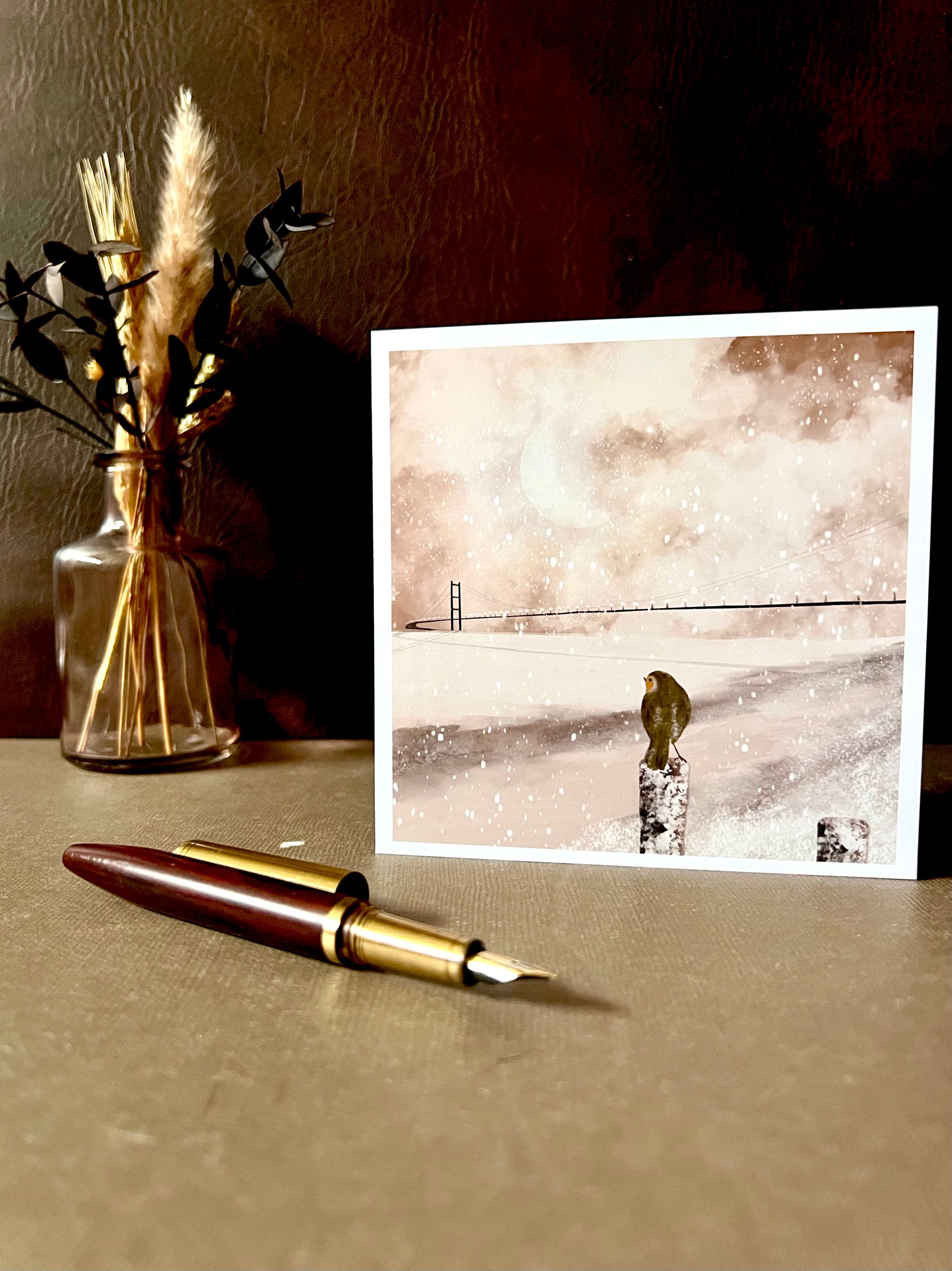 Robin perched by the River Humber with the Humber Bridge in the background, designed as a winter scene card that can be used as a Christmas card representing East Yorkshire.