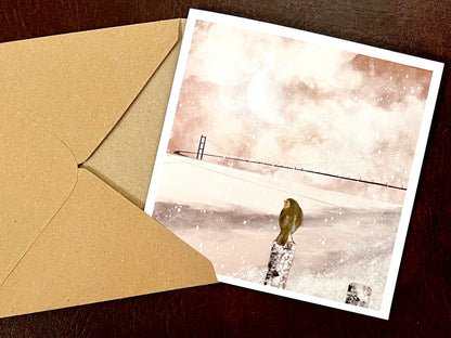 Close-up of a robin perched in a winter scene overlooking the River Humber, with the Humber Bridge softly visible in the background on a pink sepia toned greeting card.