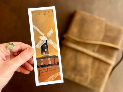 Hand holding a handcrafted Skidby Windmill bookmark featuring a countryside landscape with burnt orange autumn sunset sky and East Yorkshire windmill illustration.