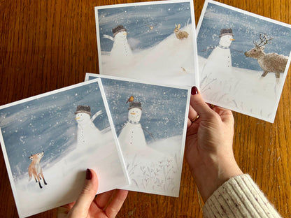 Hands holding a selection of four artisan Christmas cards featuring snowman-themed designs, shown in a fan-shaped display to highlight the festive winter collection.