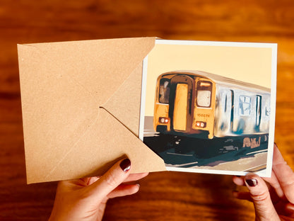 Aerial view of hands holding an artisan greeting card being removed from a high quality kraft envelope, showing the front design of the card as it is being viewed and handled.