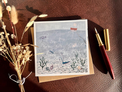 Special illustrated greeting card featuring a blue lobster and blue prawn in a crystal blue underwater coastal scene with a small boat above the water, laid flat and styled with a fountain pen and dried flowers. Joyful summery coastal art greeting card suitable for birthdays or keeping in touch.