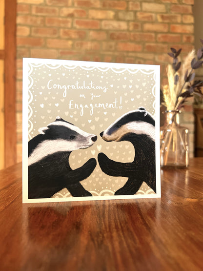 Card with two badgers facing each other and 'Congratulations on your Engagement!' text, placed on a wooden surface.