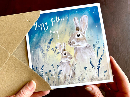 Handcrafted Father’s Day greeting card featuring an illustrated father rabbit and young rabbit sitting together in foliage under a starry blue and green night sky. The front text reads “Happy Father’s Day”. Premium illustrated wildlife greeting card with nature-inspired magical design and recycled kraft envelope.