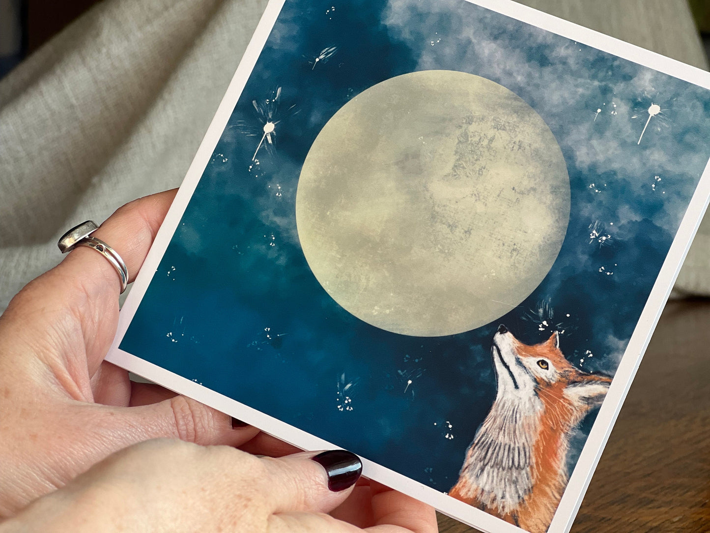 Close up of a special illustrated greeting card featuring a fox looking up at a full moon in a magical, mystical blue starry night sky design. Premium wildlife art greeting card highlighting detailed illustration and handcrafted finish.