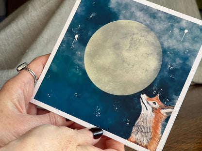 Close up of a special illustrated greeting card featuring a fox looking up at a full moon in a magical, mystical blue starry night sky design. Premium wildlife art greeting card highlighting detailed illustration and handcrafted finish.