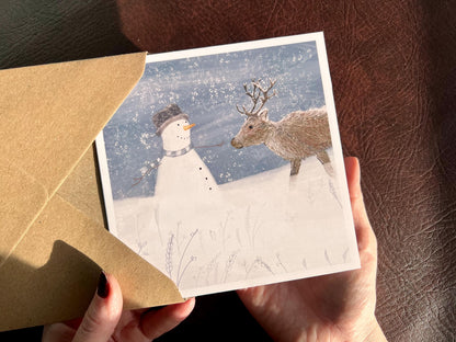 Special illustrated Christmas greeting card featuring a happy snowman looking at a reindeer in a snowy winter landscape. Festive wildlife-inspired seasonal greeting card design.