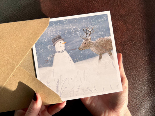 Special illustrated Christmas greeting card featuring a happy snowman looking at a reindeer in a snowy winter landscape. Festive wildlife-inspired seasonal greeting card design.