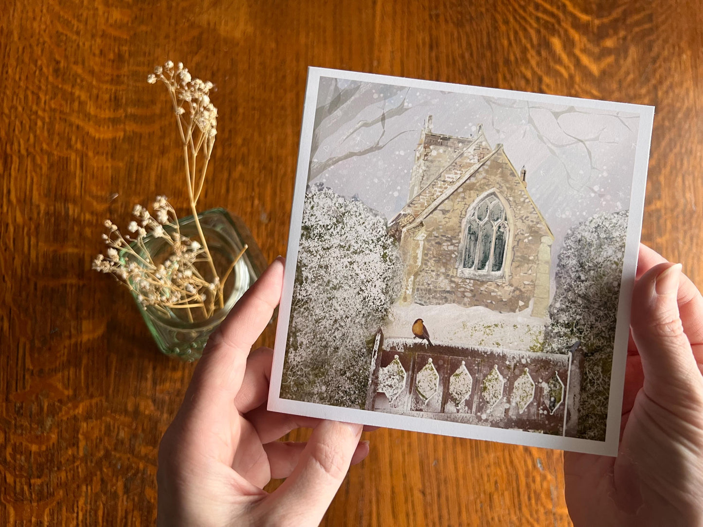 Premium Christmas card featuring St Margaret’s Church in Long Riston, East Yorkshire, illustrated in a snowy winter scene with a robin perched on a snow-covered gate. The traditional countryside church scene is shown in close-up being held towards the camera. Ideal Christmas card for Yorkshire locals, countryside lovers, church scene collectors and robin enthusiasts. Printed on thick 312gsm fine art card by a UK independent artist.