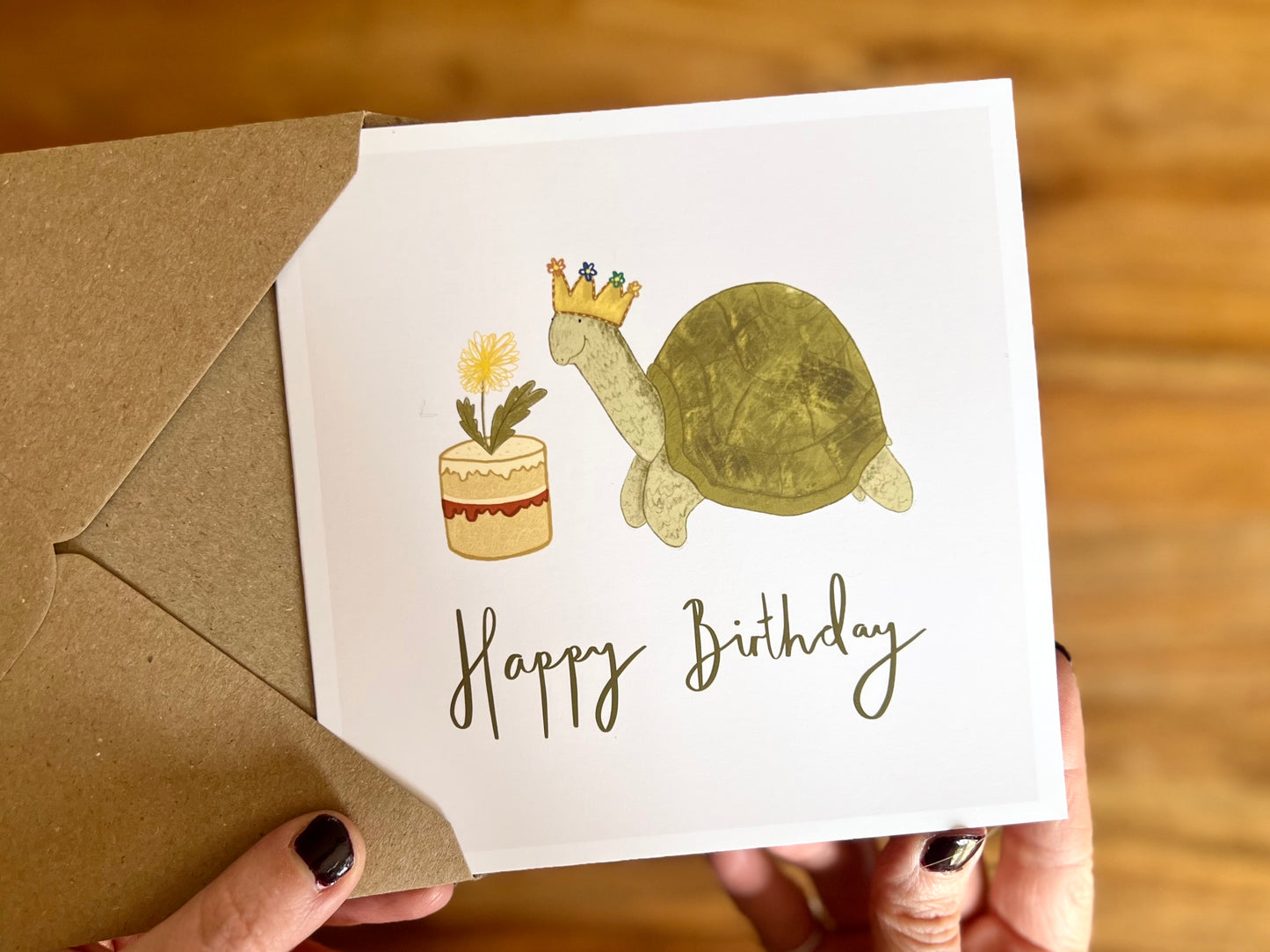 Premium birthday card featuring a playful illustrated tortoise wearing a birthday crown and eating a dandelion cake. The cartoon-style design sits on a plain white background with the text ‘Happy Birthday’ underneath. Ideal birthday card for tortoise owners, reptile lovers or animal enthusiasts. Printed on thick 312gsm fine art card by a UK independent artist and supplied with a recycled kraft envelope.