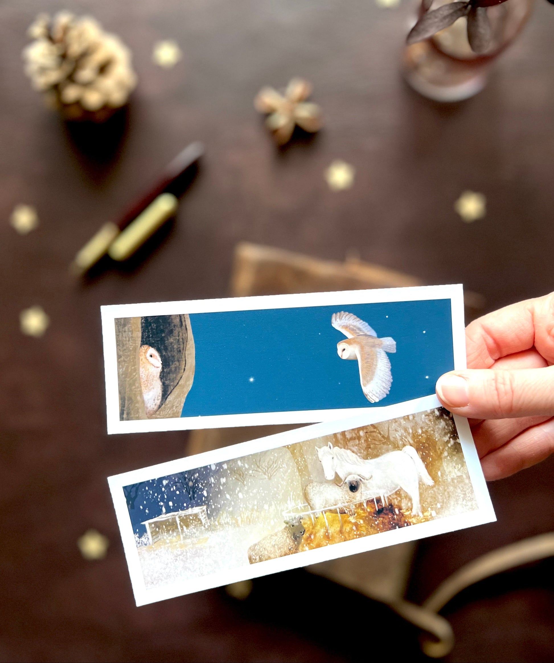 Close-up of handmade wholesale bookmarks featuring original nighttime animal illustrations, including a barn owl and owlet and a snowy horse with sheep, designed and made in East Yorkshire.