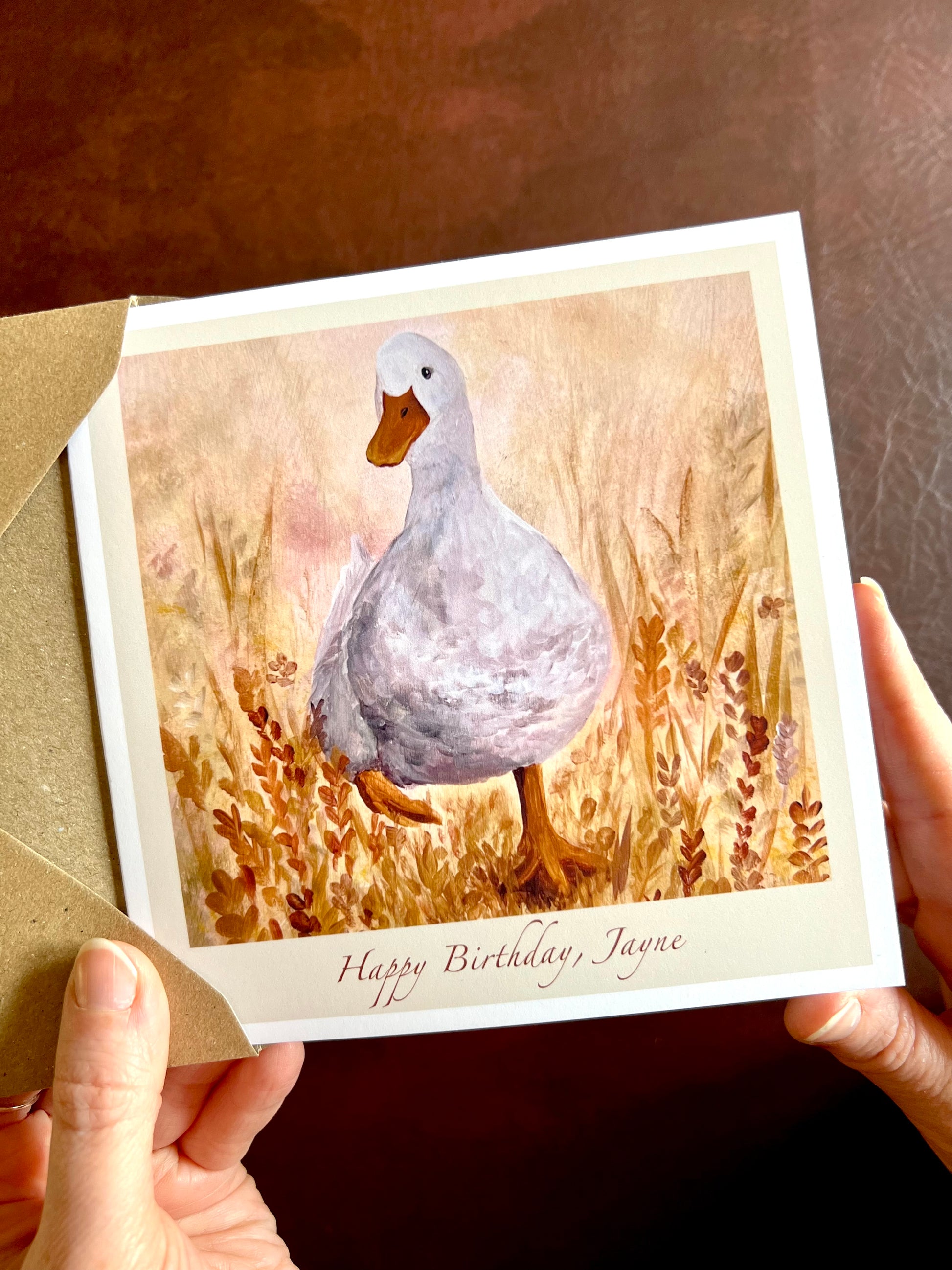 Close-up of Duck in the Meadow birthday card being removed from a 110gsm recycled fleck kraft envelope, showing personalised text option ‘Happy Birthday, [Name]’