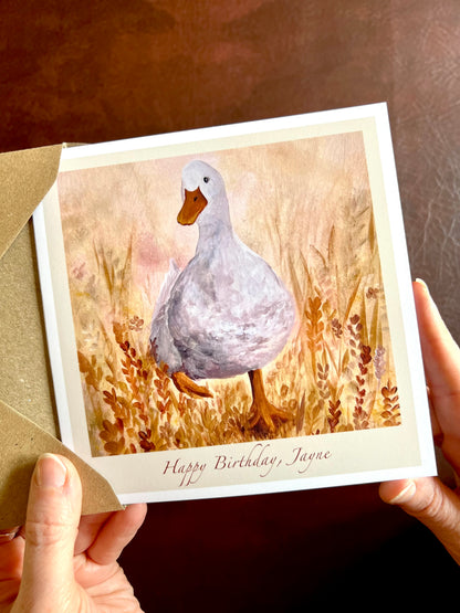 Close-up of Duck in the Meadow birthday card being removed from a 110gsm recycled fleck kraft envelope, showing personalised text option ‘Happy Birthday, [Name]’