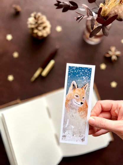 Illustrated bookmark featuring a red fox beneath a snowy night sky. Woodland themed background with sketchbook, pine cones, and kraft paper stars. Part of a 16 pack animal bookmark set for wedding favours.