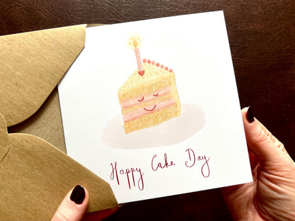 Hands holding Happy Cake Day birthday card without personalisation, coming out of 110gsm recycled kraft envelope, UK handmade