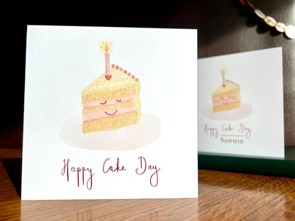 Cheerful Happy Cake Day birthday card with smiling cake illustration standing on wooden tabletop, non-personalised option shown, UK handmade