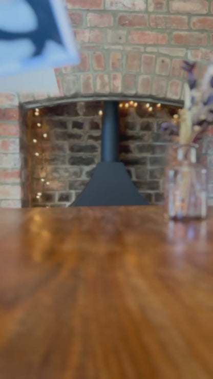 Slow pan video showing a range of personalised engagement card designs placed one at a time on a rustic wooden table, in front of a farmhouse-style brick fireplace with warm fairy lights in the background, featuring illustrated badger designs and gender-neutral congratulations cards suitable for Mr & Mr, Mrs & Mrs or Mr & Mrs couples, including son and daughter in law gifting options