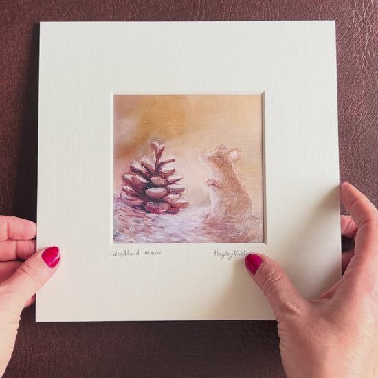 Video showing the Woodland Mouse mounted art print being lifted from a brown leatherette surface and held up for a close-up view of the artwork details, before being turned over to display the mount board backing and artist logo stamp on the reverse.