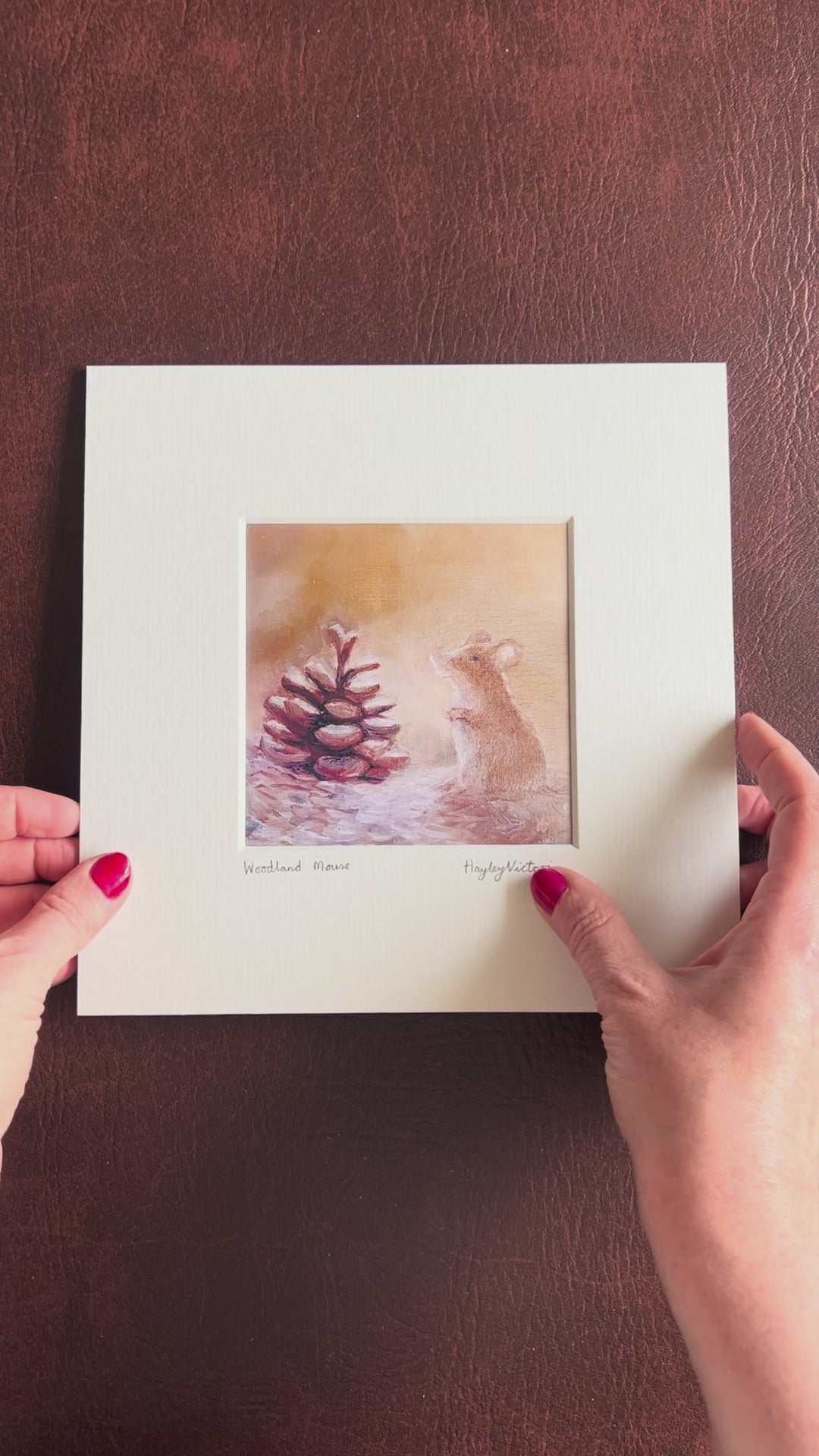 Video showing the Woodland Mouse mounted art print being lifted from a brown leatherette surface and held up for a close-up view of the artwork details, before being turned over to display the mount board backing and artist logo stamp on the reverse.